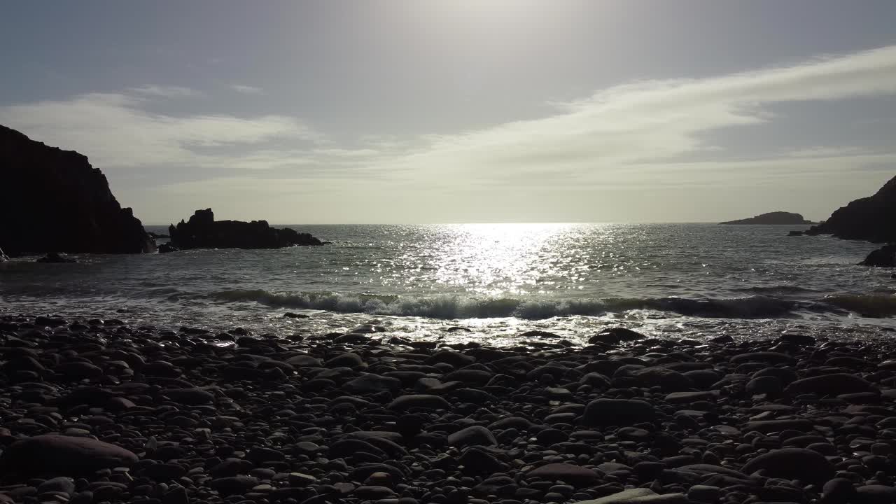 바위 모래 해변에 있는 평온한 바다와 바다에 반사되는 밝은 태양