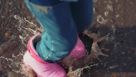 active-child-in-pink-rubber-boots-jumps-in-puddle-in-park