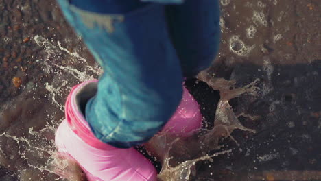 active child in pink rubber boots jumps in puddle in park