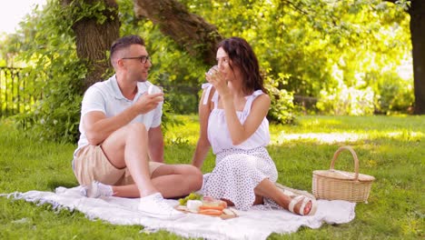 Happy-Couple-with-Food-Having-Picnic-on-Beach.leisure,-relationships-and-people-concept-happy-couple-with-food-eating-grapes-and-having-picnic-on-beach