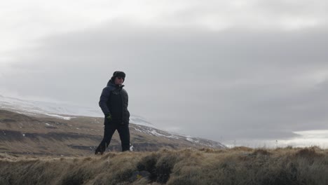 Tourist-walk-in-cloudy-Icelandic-landscape-with-huge-mountain-in-background