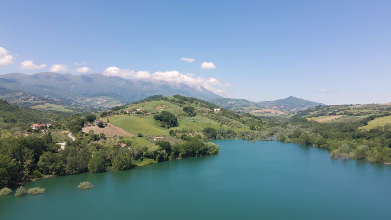 Ripresa aerea grandangolare con drone di una splendida vista panoramica di un lago color smeraldo situato in una valle circondato da una catena montuosa e terreni agricoli nella campagna abruzzese in Italia.