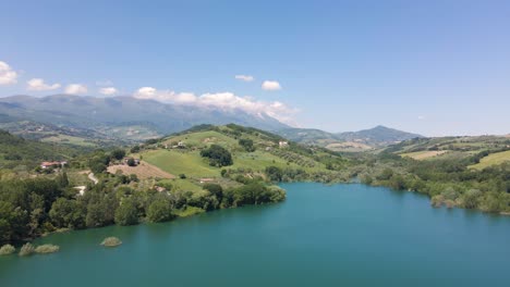 toma de un dron de gran angular de una hermosa vista panorámica de un lago esmeralda ubicado en un valle rodeado por una cordillera y tierras de cultivo en el campo de abruzzo en italia