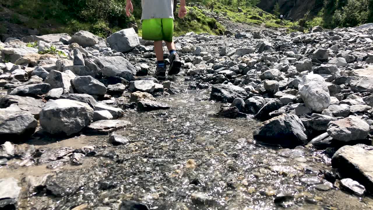 lindo niño caminando y jugando con piedras en el río de montaña que viene de una cascada