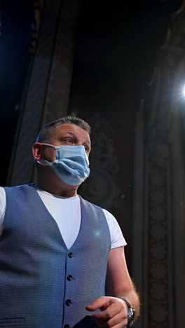 actor in elegant suit and medical mask. actor in protective facial mask standing on stage of a theater. coronavirus and pandemic concept. vertical video