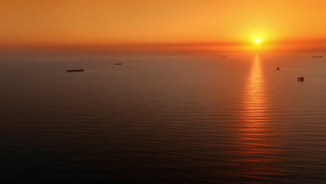 orange sky with setting sun above the vast waterscape. some ships are standing on the anchor. amazing view of the sea or ocean at sunset.