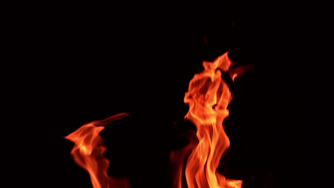 Tongues of orange flame rising up high. Tiny glaring sparkles fly up from bonfire. Black backdrop.