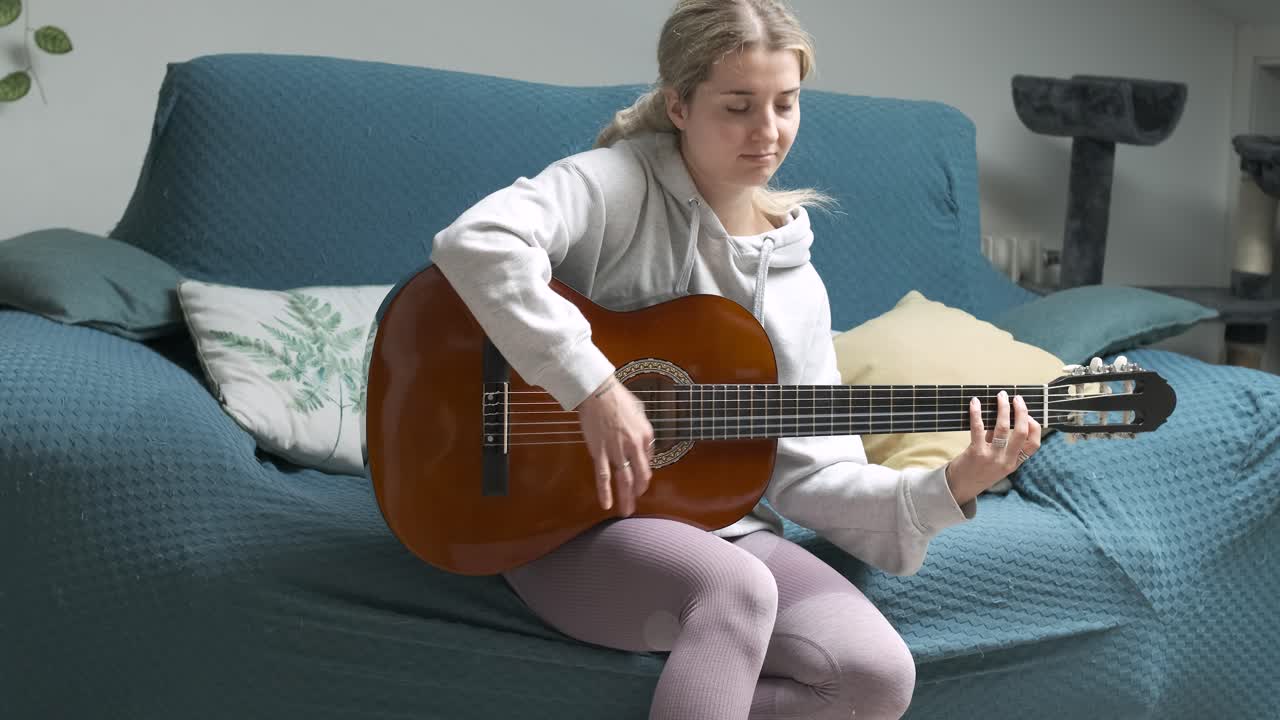 Young woman enjoying guitar practice on a comfortable sofa