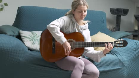young woman enjoying guitar practice on a comfortable sofa