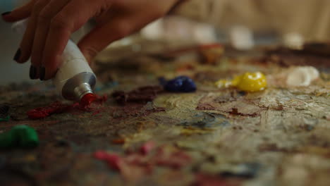 Unrecognizable-woman-squeezing-red-paint-inside.-Painter-preparing-workplace.