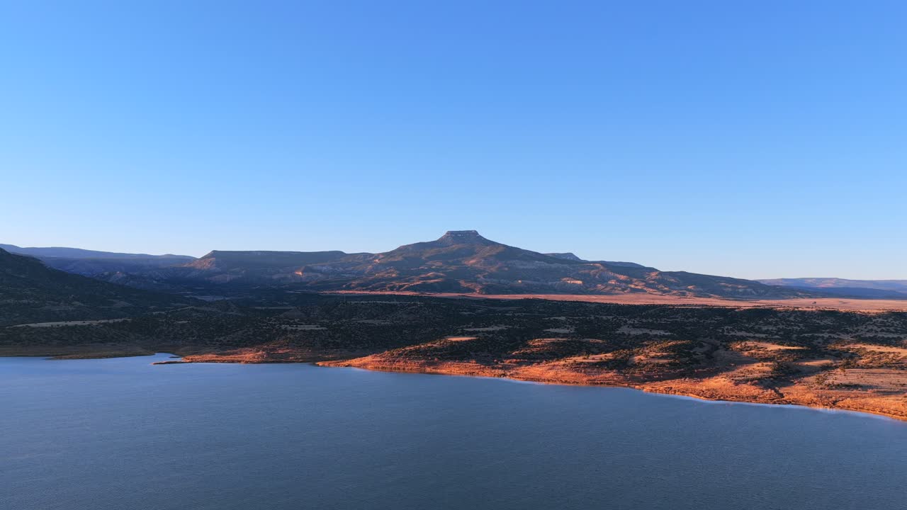 High desert landscape features the volcanic basalt peak of Cerro Pedernal above Abiquiu Lake reservoir. The arid plateau geology of New Mexico offers a stunning background for cinematic travel film