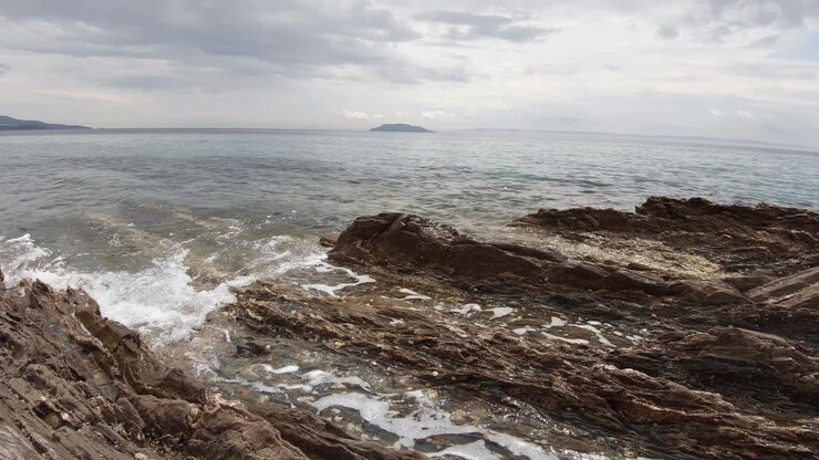 Inquadratura paesaggistica di onde che si infrangono su una costa rocciosa in Grecia in una giornata di sole.