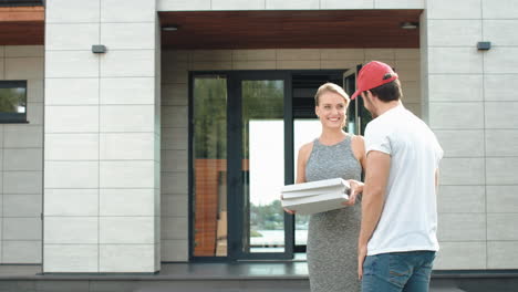 Joven-Mensajero-Entregando-Pizza-A-Una-Casa-De-Lujo.-Mujer-Sonriente-Tomando-Cajas-De-Pizza