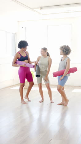 vertical video: diverse group of women holding yoga mats, smiling and chatting in studio