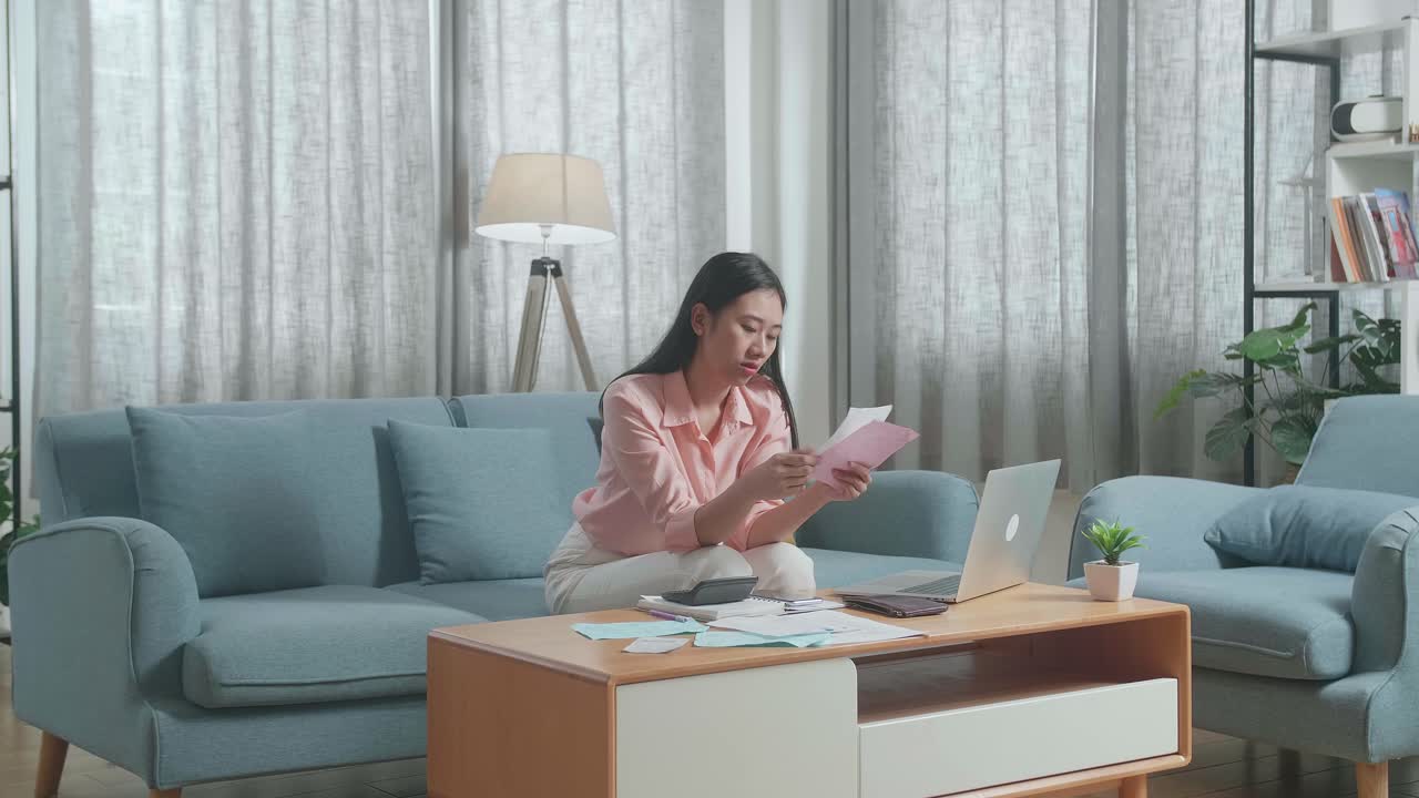 노트북을 가진 아시아 여성이 청구서를 보고 재정 문제로 인해 두통을 고 있습니다.