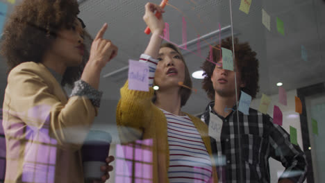 Diverse-work-colleagues-using-memo-notes-and-writing-on-glass-wall-having-a-discussion