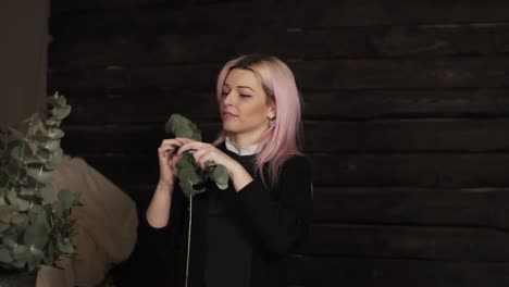 an attractive, happy girl with pink hair removes a handful of green leaves from a branch and playfully throw at the camera