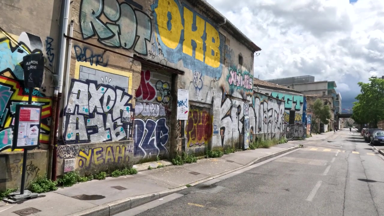 En långsam kamerapanorering fångar livfulla graffitimålningar på gamla byggnader längs en gata.