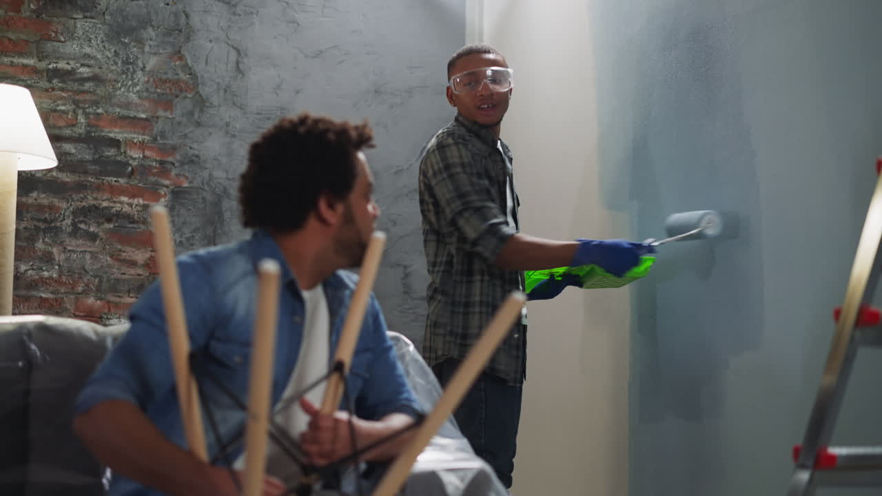 un hombre afroamericano alegre pinta una pared hablando con su hermano.