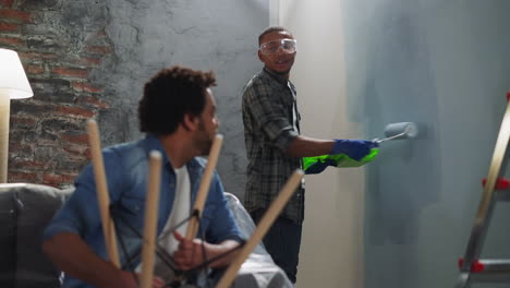 cheerful african-american man paints wall talking to brother