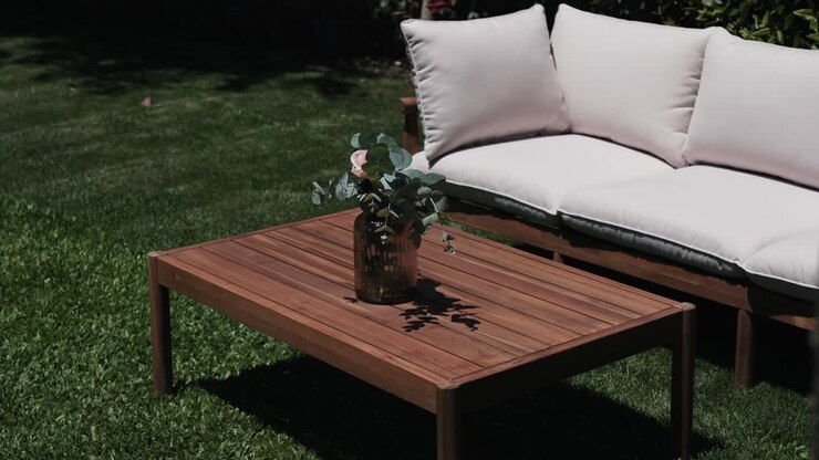 Tavolo in legno da esterno con un vaso di foglie di eucalipto accanto a una morbida panca imbottita alla luce del sole