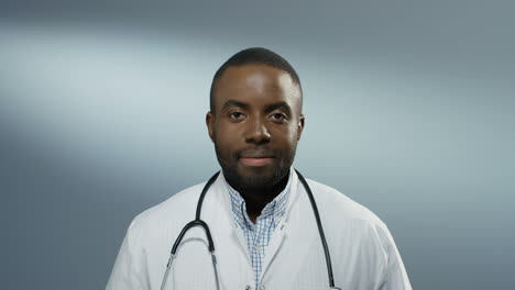 Primer-Plano-Del-Joven-Médico-O-Pasante-Feliz-Sonriendo-Alegremente-A-La-Cámara-En-El-Fondo-De-La-Pared-Gris