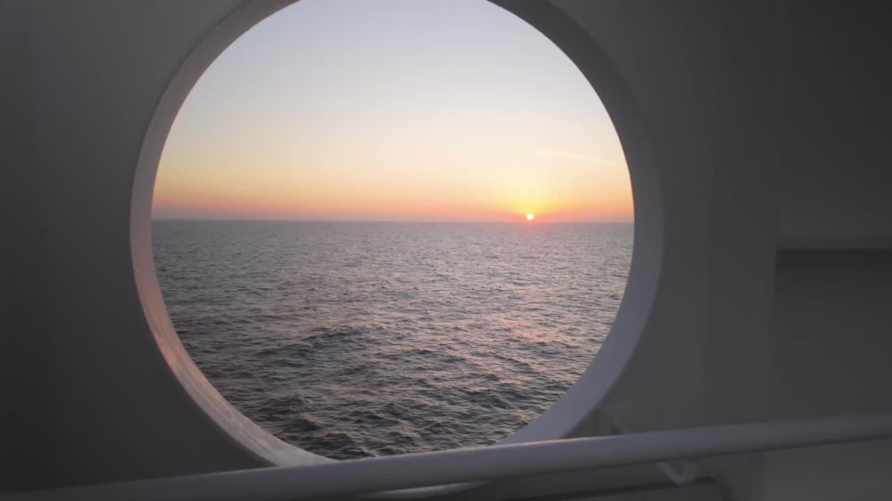 Ein ruhiger Sonnenaufgang, gesehen durch ein Bullauge eines Schiffes. Der ruhige Ozean und das sanfte Morgenlicht schaffen einen friedlichen Start in den Tag an Bord und fangen die stille Schönheit des Reisens auf See ein.
