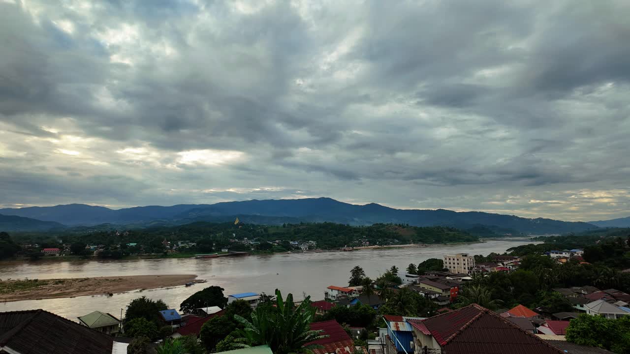 Ampia ripresa statica in timelapse di Houayxay, in Laos, con vista sul fiume Mekong verso la Thailandia, con nuvole che si muovono sopra le montagne, la città sul fiume e il paesaggio di confine che creano un'atmosfera cinematografica calma