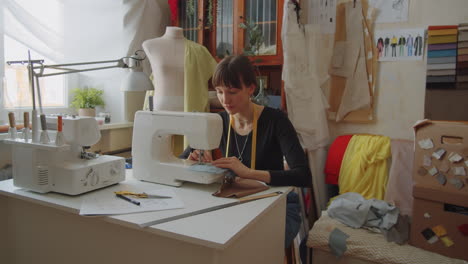 woman stitching fabric on sewing machine in dressmaking studio