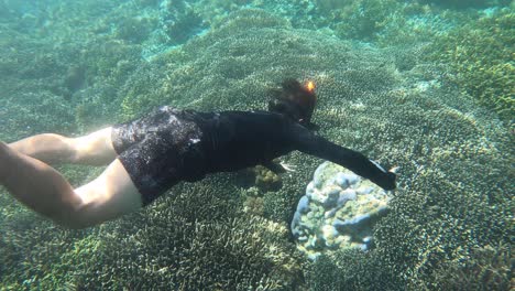 pov shot of young attractive man diving down and snorkeling in tropical ocean water with beautiful coral reef