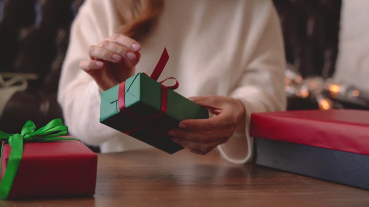 vista de cerca de las manos de la mujer envolviendo un regalo de navidad con un lazo en una mesa 1