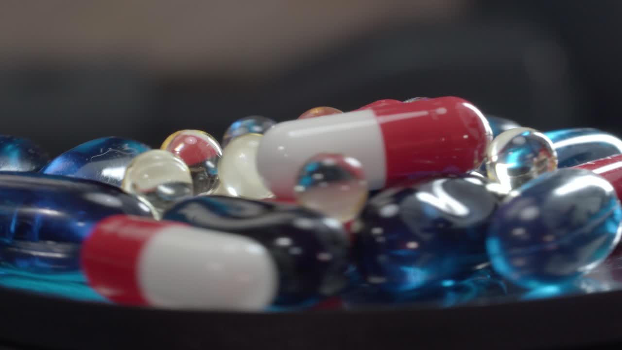 Close up of assorted capsules and transparent softgel pills rotating on reflective surface, studio shot