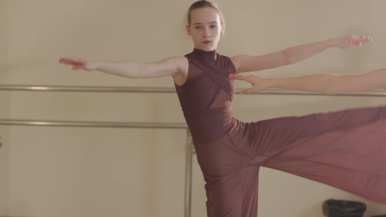 검은색 댄스웨어를 입은 젊은 발레 학생들이 나무 바닥과 벽에 장착된 바를 가진 넓은 발레 스튜디오에서 자세를 연습하는 그룹.