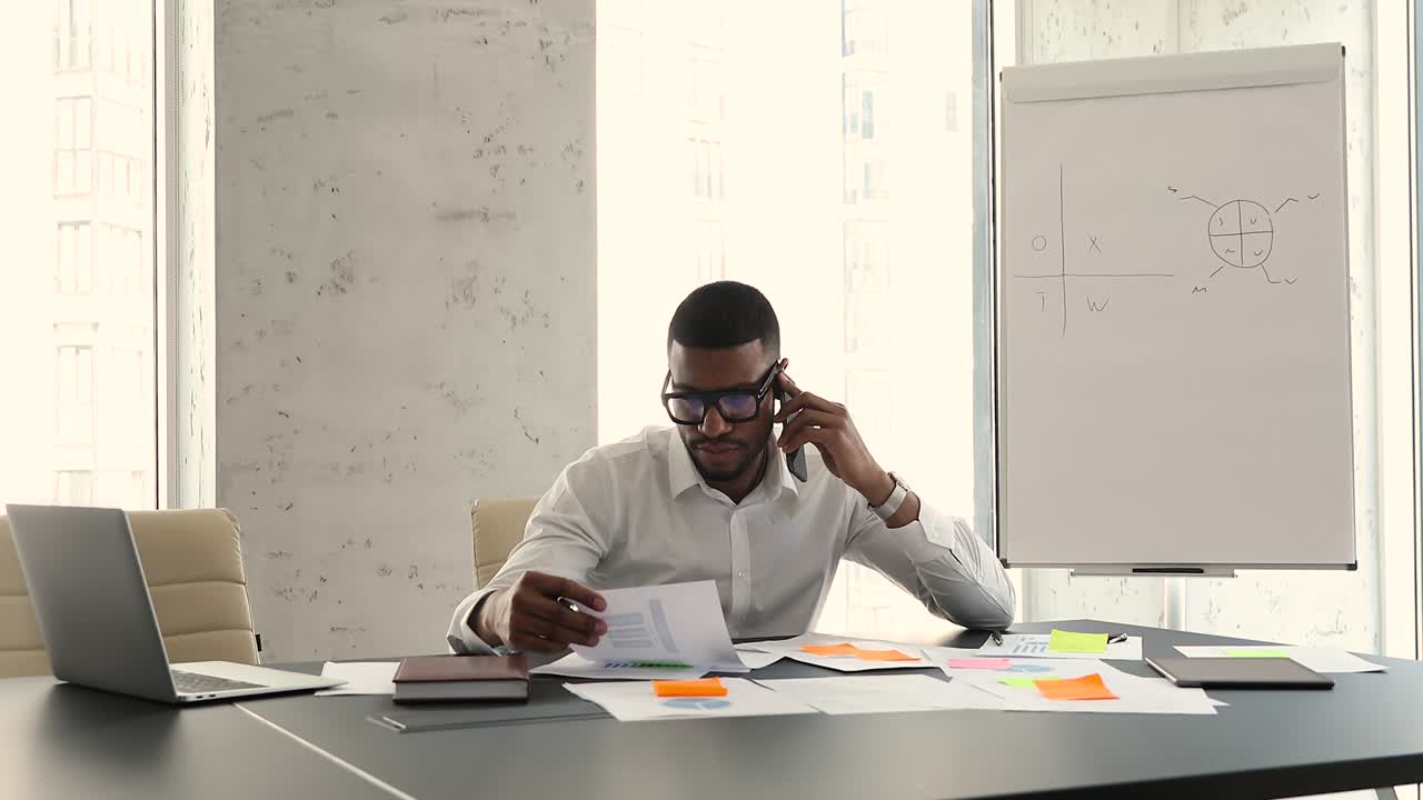 African businessman talks on cellphone discuss paperwork, use laptop