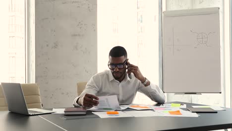 african businessman talks on cellphone discuss paperwork, use laptop