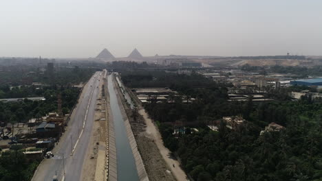 aerial shot track out and rising up for the pyramids of egypt in giza in the background of a branch of the river nile in the foreground maryotya branch showing greenery in the surroundings