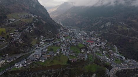 Relaxed-Forward-flying-drone-video-downwards-tilting-in-Swiss-Alps-valley-on-moody-grey-winter-afternoon-with-lush-pine-forests-and-clouds-in-mountains