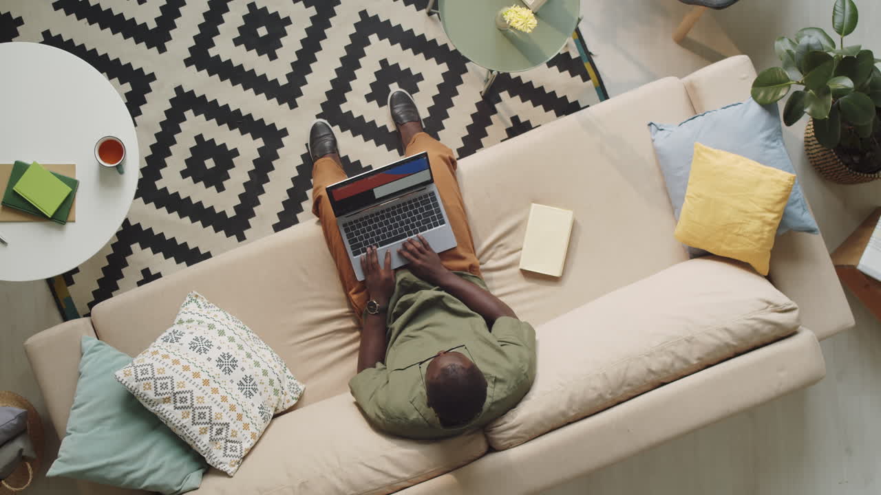 Black Man Using Laptop on Sofa in Living Room