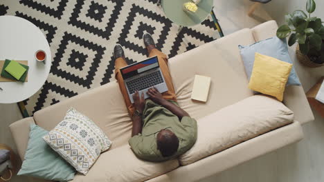 black man using laptop on sofa in living room