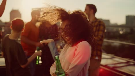 vista de cerca de una mujer afro bailando con una bebida en una discoteca al atardecer