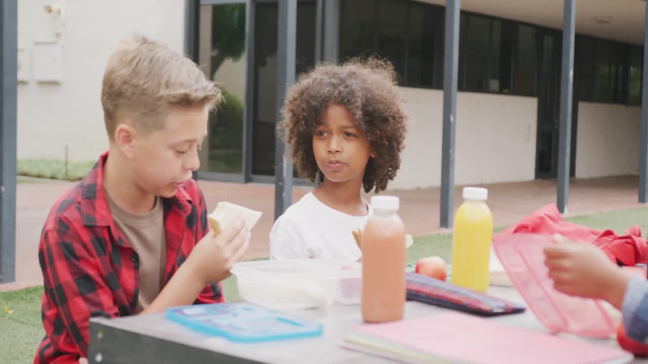 Video di due studenti di diverse etnie che mangiano il pranzo al sacco e parlano nel cortile della scuola