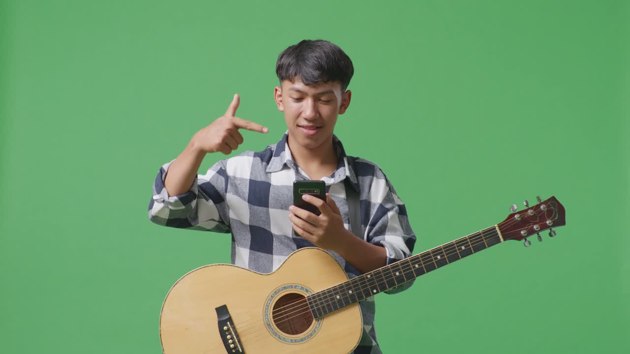 초록색 스크린 배경에서 손에 스마트폰을 가리키는 기타를 들고 있는 아시아 십대