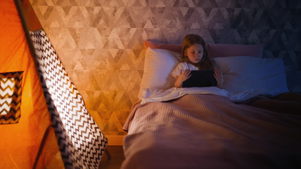 작은 아이가 놀이 텐트  ⁇ 에 침대에 누워 만화를 보고 있습니다.