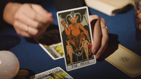 close up of woman giving tarot card reading on candlelit table holding the devil card 3