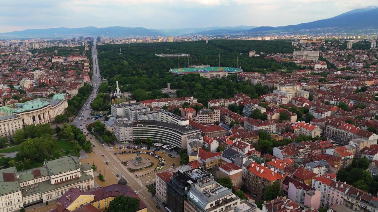 Amplia vista aérea que domina los tejados históricos de la ciudad y los parques urbanos verdes de Sofía, Bulgaria. Toma de seguimiento de paisaje urbano con dron durante el día bajo un cielo despejado.