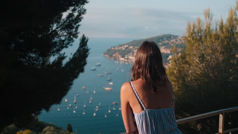 Close-up-dolly-shot-of-pretty-brunette-girl-enjoying-beautiful-sunset-view-of-lighting-ocean-with-boats-and-coastline-in-background