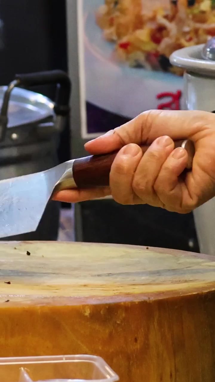 Una persona che indossa guanti affila con cura una grande lama di metallo su una spessa tavola di legno