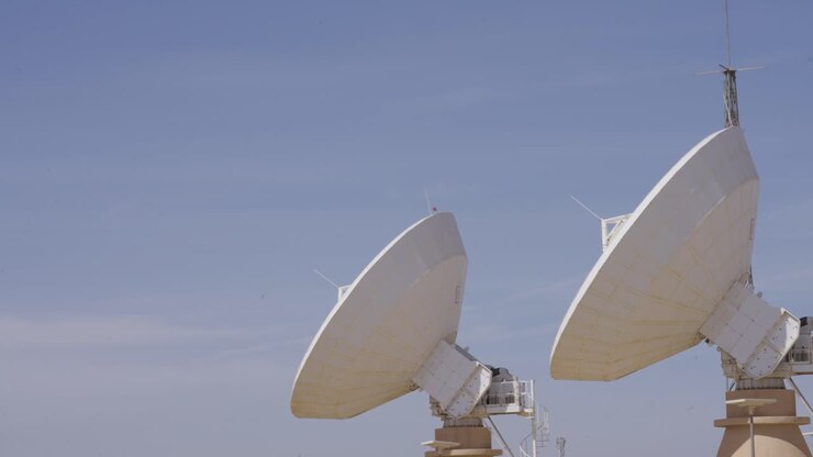 Large parabolic satellite dishes at a telecommunications ground station point to the clear blue sky. A symbol of global communication, data transmission, and modern technology