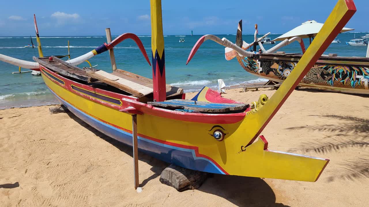 Tradizionale barca da pesca a bilanciere dipinta con colori vivaci e occhi sulla prua ormeggiata sulla spiaggia di Sanur, Bali, Indonesia