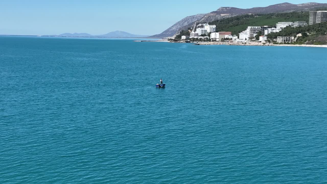 pescador solitario tira del barco a lo largo de la línea en el agua en un día soleado cerca de la costa